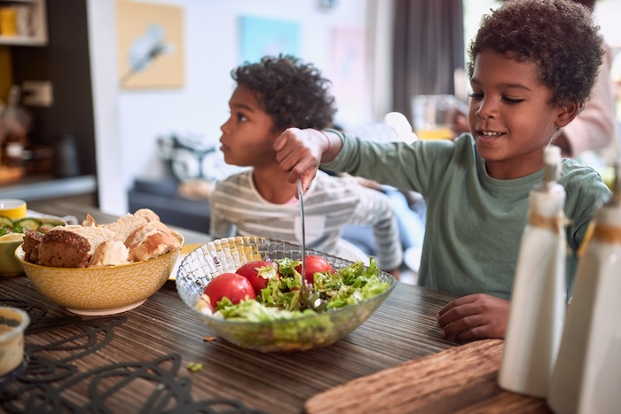 Young black child preparing a salad with his family in the kitchen.