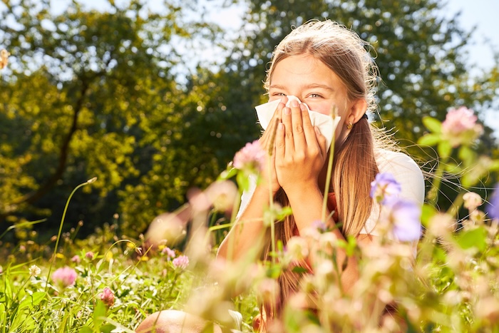 Teenage girl blowing her nose in a grassy field.