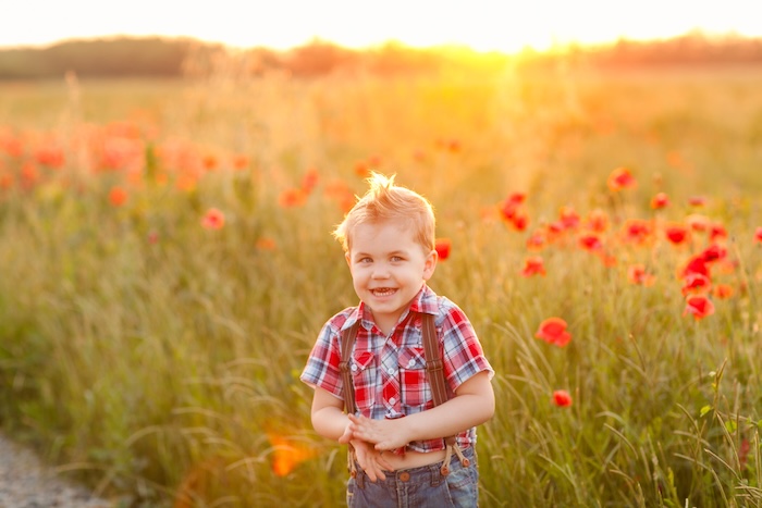 Young happy child standing in front of a field of grass at sunset. 