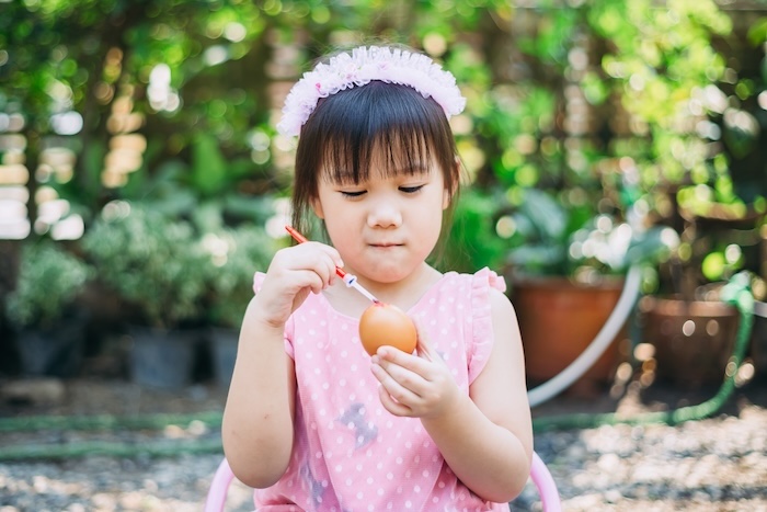 Young Asian child painting an Easter Egg in a park. 