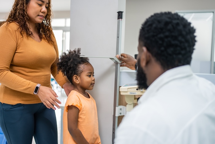 Black male doctor measuring a child’s height at the pediatric office.
