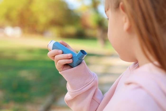 Young redhead girl using an inhaler outside in a park. 