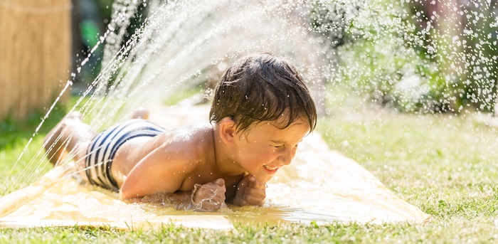 Young boy playing on a slip-and-slide on a hot summer day.
