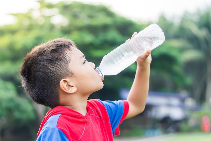 Young Asian boy drinking cold water at a sports practice on a hot summer day.