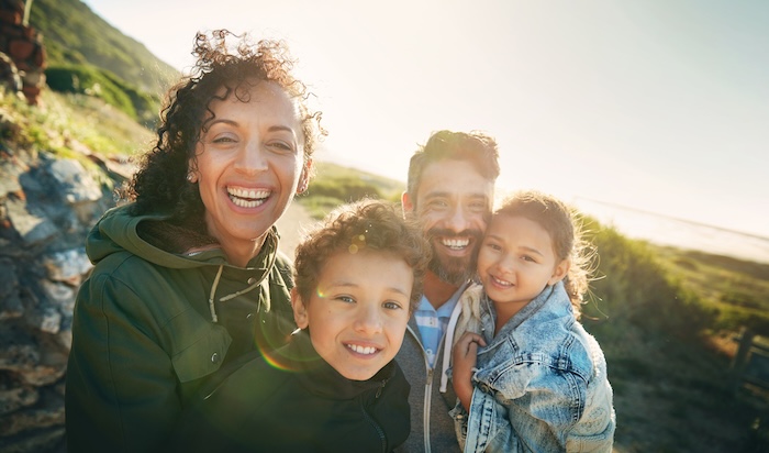 Ethnically ambiguous family on vacation walking along a grassy hillside.