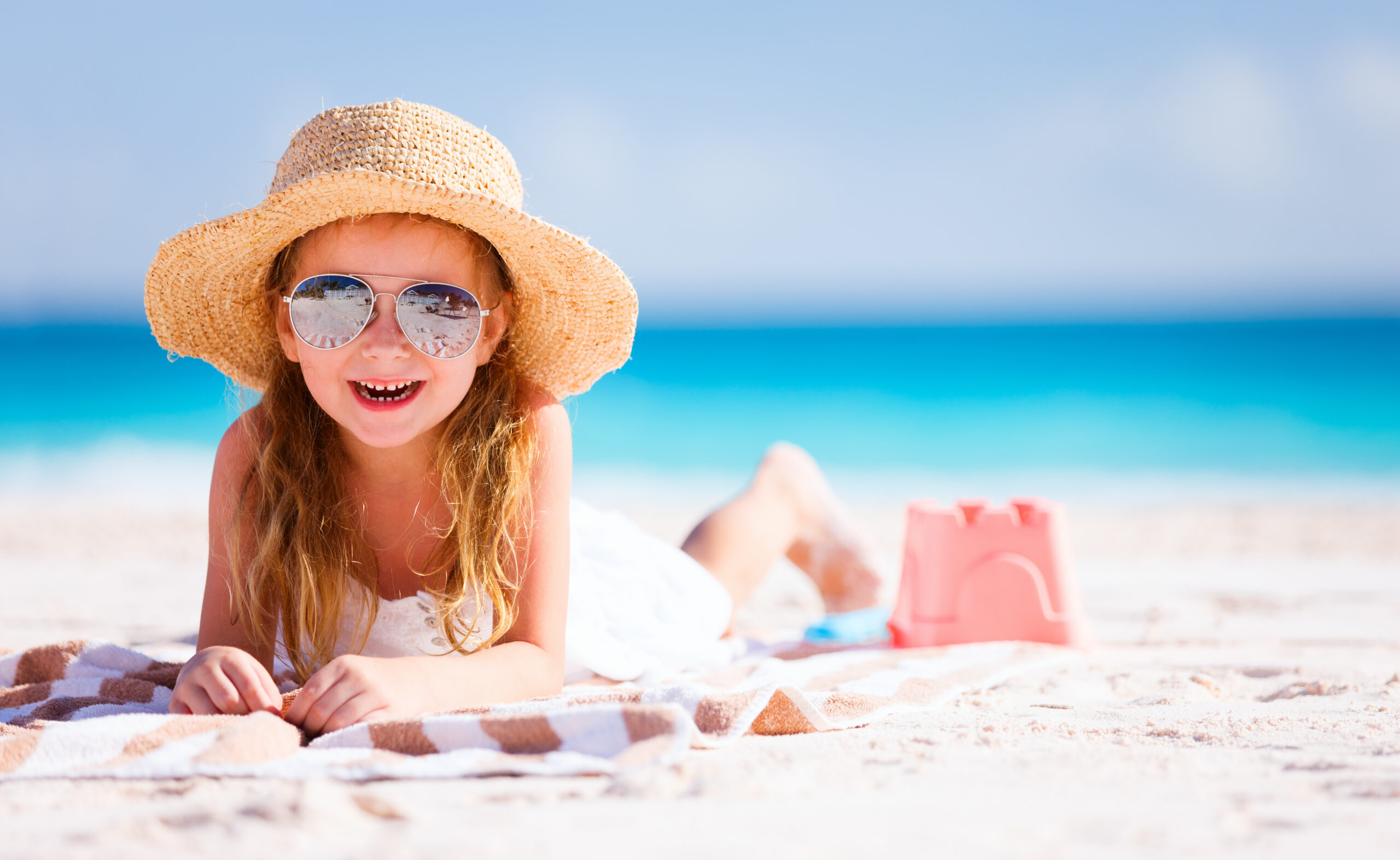 Smiling young girl at the beach, wearing a hat.