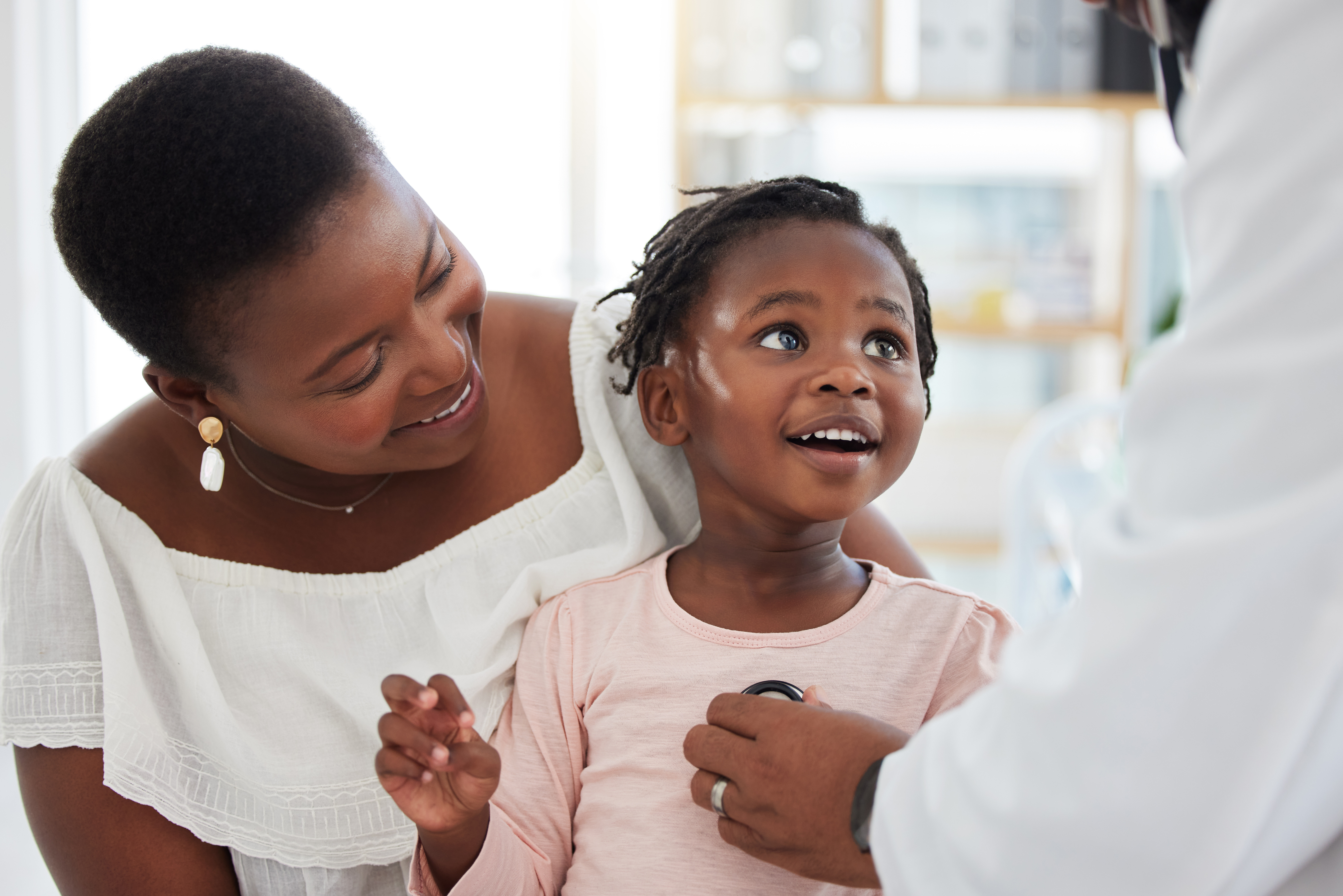 Smiling black child being held by her mother at the pediatrician’s office.