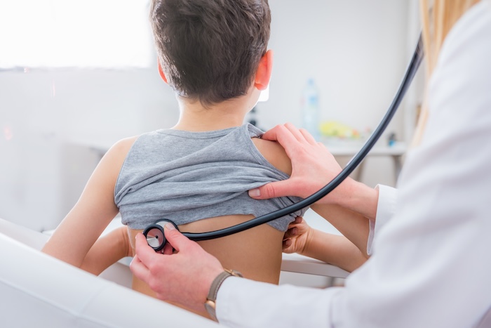 Young boy lifting his shirt at a pediatric appointment.