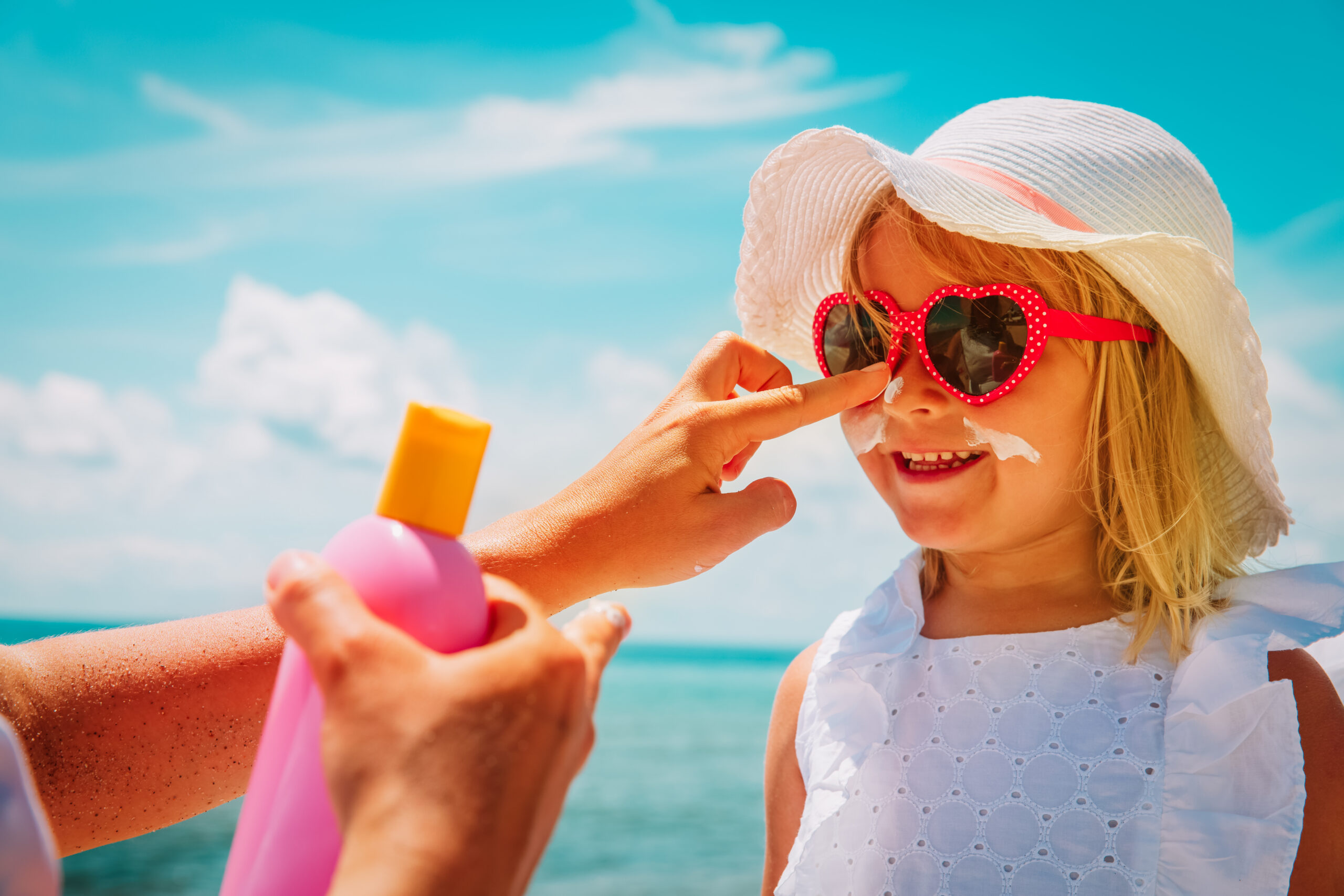 Mother applying sunscreen to her young daughter at the beach.