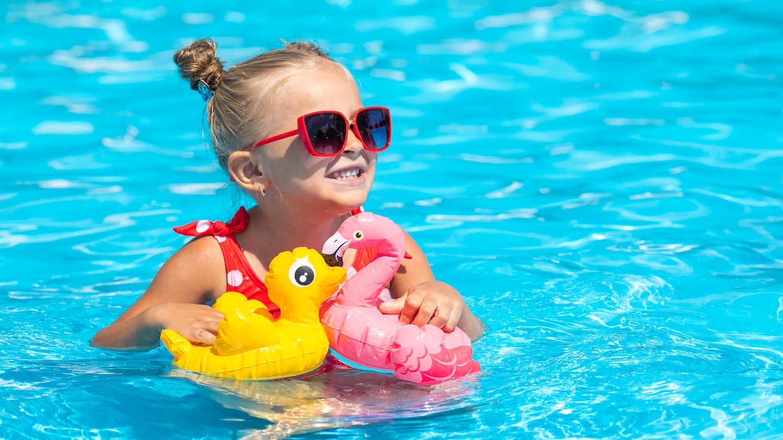 Young girl smiling with floaties in the pool.