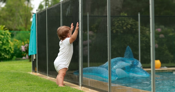 Baby standing up against a pool fence at home.