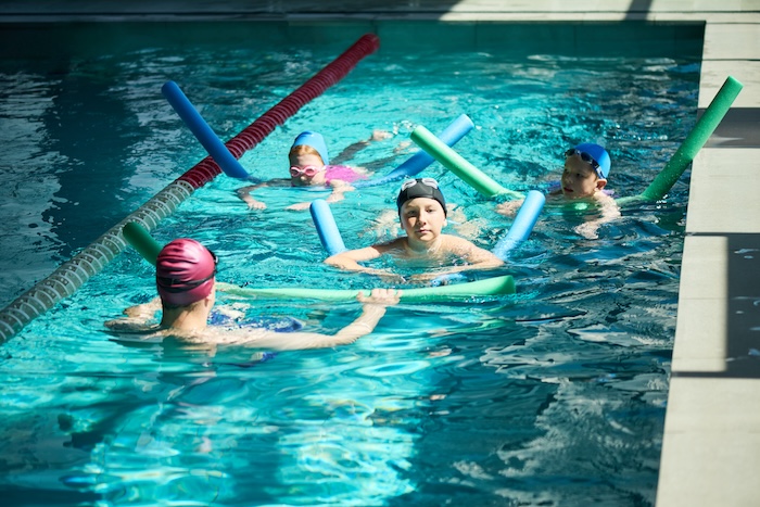 Young kids in a pool taking swimming lessons.