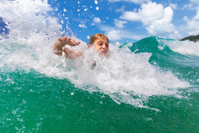 Preteen boy body surfing at the beach.