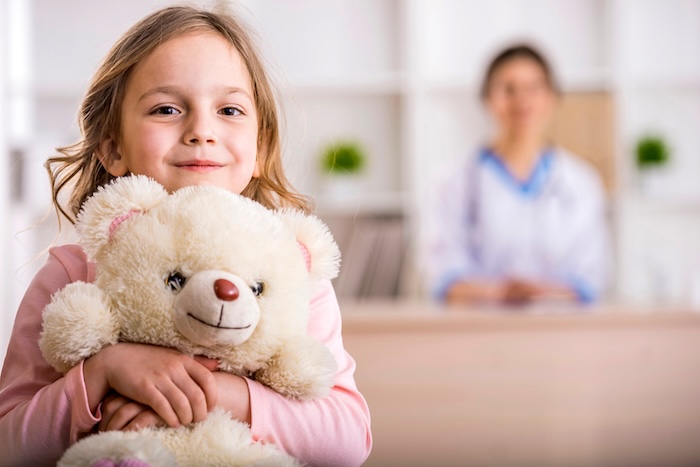 Girl holding a teddy bear in her pediatric office. 