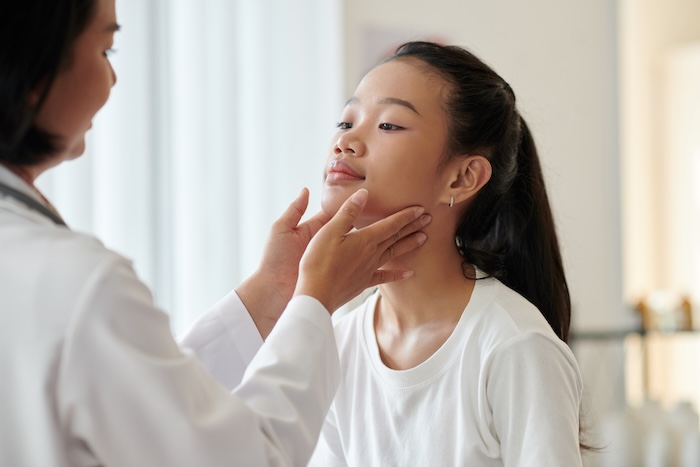 Female pediatrician examining the face of an Asian teenage girl during a well child exam.

