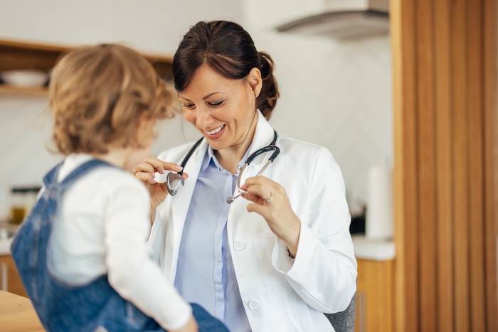 Caucasian female pediatrician showing a little boy patient her stethoscope.