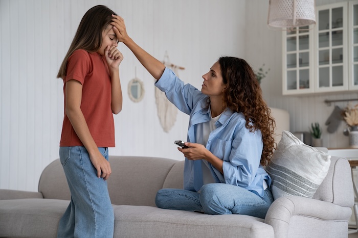 Ethnically ambiguous mom feeling her sick pre-teen daughter’s forehead for a fever.