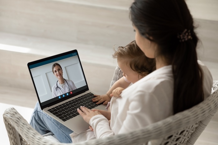 Young mom with her baby on a video call telehealth appointment with her pediatrician.